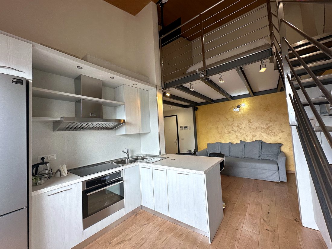 Il soggiorno del loft MO&VI con cucina, travi nere a vista e scala in acciaio