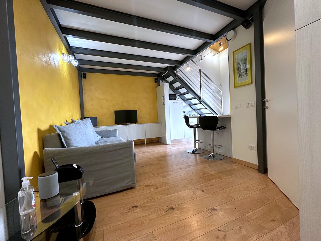 Zona giorno del loft con divano, parete color ocra e travi nere