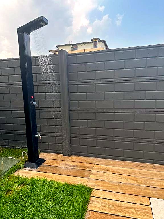 Doccia esterna nera sul camminamento in legno accanto al prato